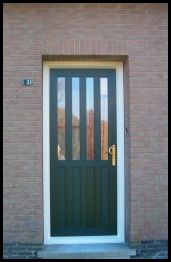Voordeur met 4 verticale stijlen en 1 horizontale stijl voor de scheiding tussen glas boven en paneel onder. Messing deur kruk